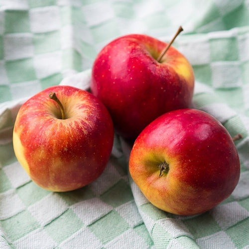 Three red apples on a green and white checkered cloth